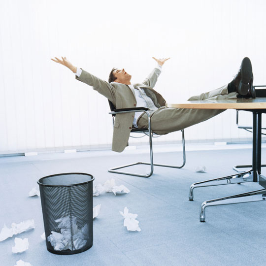 Man leaning back in chair with legs up on desk and arms up in the air.